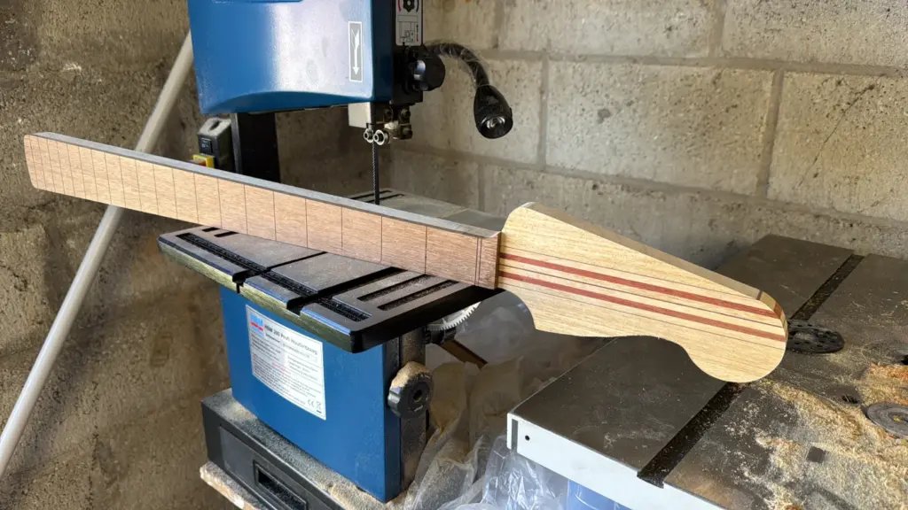 Manico laminato a strisce di ramino e padouk posizionato sulla sega a nastro prima del taglio di sagomatura