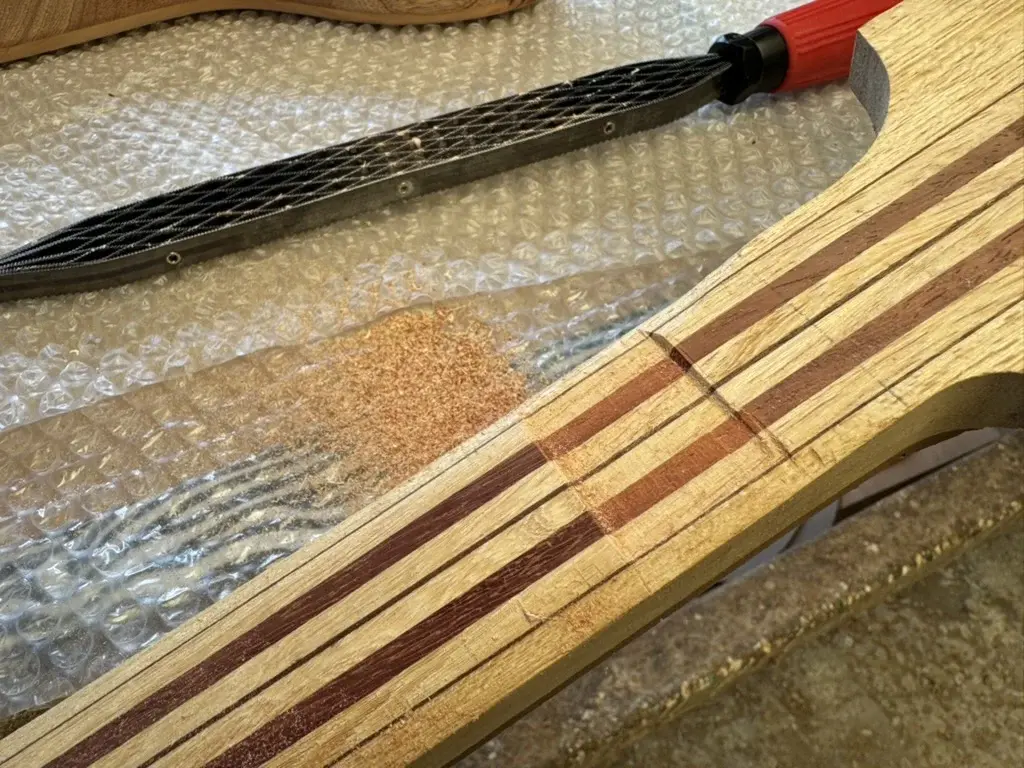 Manico multi-lamina in ramino e padouk del Precision Bass con il riferimento di profilo stabilito al primo tasto tramite raspa Shinto, prima della sagomatura completa con la vastringa