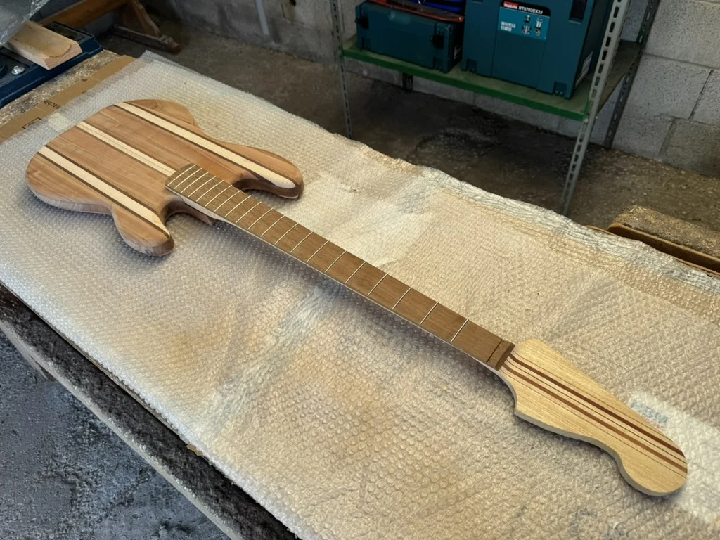 Vista dall'alto del Precision Bass artigianale con body e manico multi-lamina in ramino, padouk e mogano, tastiera in iroko con tasti già battuti, su piano di bolla bianco